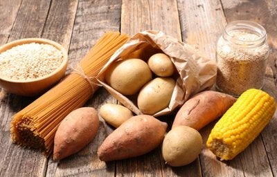 Alimentos ricos em amido como batata, batata-doce, milho, massas e grãos dispostos sobre mesa rústica.