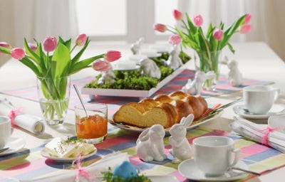Decoração de Páscoa: Mesa decorada com pratos, talheres, pães, vaso com flores e xícaras