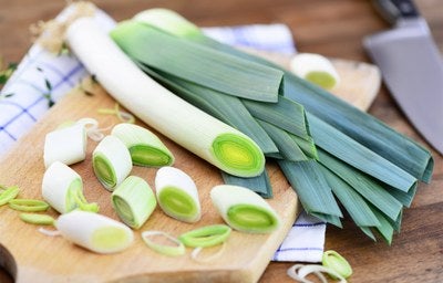 Alho-poró inteiro e fatiado sobre uma tábua de madeira, mostrando o ingrediente fresco para preparo de receitas.