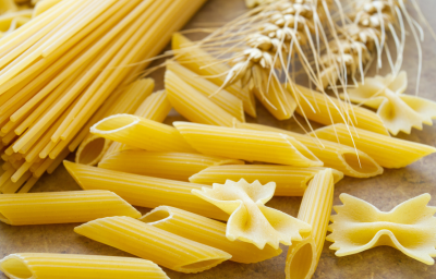 Massas secas italianas dos tipos espaguete, penne e farfalle com espigas de trigo em composição culinária.
