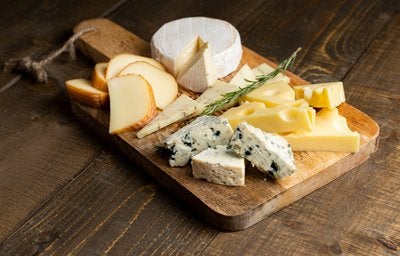 Tábua de madeira com variedade de queijos, incluindo brie, queijo azul, suíço e defumado.