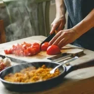 Comida italiana: uma pessoa cortando tomate em cima da tábua de madeira