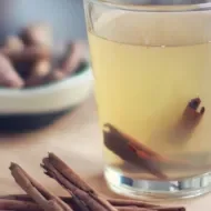 Chá de Gengibre: chá de gengibre em uma xícara, com canela dentro e em volta da xícara, em cima de uma mesa de madeira