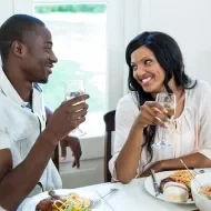 Almoço Romântico:Um homem negro à esquerda com um copo na mão, à direita uma mulher negra com um copo na mão