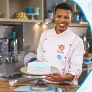 Imagem de um rapaz com uniforme branco com um bolo decorado em tons azul os dizeres com o nome do curso e os logos