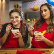 Imagem de duas meninas vestidas de vermelho, segurando taças com a receita e os dizeres com o nome do vídeo e da receita