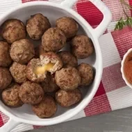Panela com vários bolinhos de carne moída recheados com queijo. À direita um molho e, abaixo, um pano xadrez (Vermelho e bran