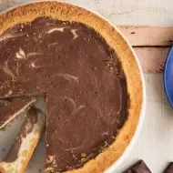 Torta de chocolate com dois pedaços cortados sobre um pano azul. À direita, pedaço de torta sobre um prato com um garfo ao la