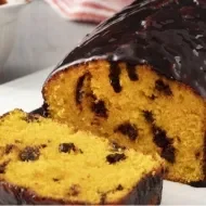Bolo de cenoura com cobertura de chocolate em cima de um prato, à esquerda pote com gotas de chocolate