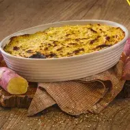 Imagem de uma receita de escondidinho, com batatas-doces ao redor, numa bancada e do lado direito o nome da receita e o logo