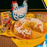 Montagem com a foto do cuscuz com atum à esquerda, o nome do programa e da receita à direita e a galinha azul no centro 