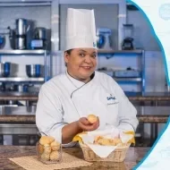 Montagem com a imagem de uma chefe com uniforme branco à esquerda e à direita o título da aula pão de queijo