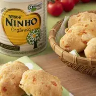 Sobre uma tábua de madeira, uma cesta e um guardanapo com pães salgados, feitos com Leite Ninho.