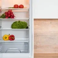 Geladeira branca aberta com legumes e alface dentro dela