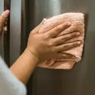 Mulher limpando a geladeira inox com um pano laranja