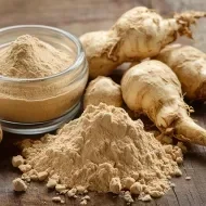 Raízes de maca peruana e pó em recipiente e montinho sobre mesa rústica de madeira.