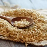 Arroz integral cru sobre tecido rústico, com colher de madeira apoiada por cima, em uma superfície de madeira envelhecida.