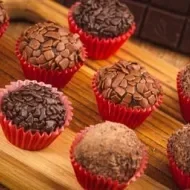 Imagem de brigadeiros de chocolate em forminhas vermelhas em uma tábua de madeira.