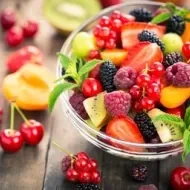 Tigela de vidro com frutas coloridas como framboesas, kiwis, cerejas, pêssego, groselha e amora.