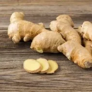 Raízes de gengibre frescas sobre superfície de madeira, com algumas fatias cortadas à frente.