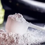 Colher medidora com creatina em pó branca sobre a mesa, ao lado de uma fita métrica amarela desfocada.