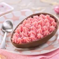 Ovo de Páscoa de chocolate ao leite recheado com Nesquik e confeitos coloridos, servido em prato decorado.
