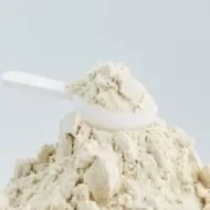 Whey protein em pó em cima de uma mesa branca, junto a um scoop. A imagem representa se whey substitui refeição.