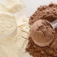 Colheres medidoras com whey protein em pó sabor baunilha e chocolate, sobre a superfície de pó.