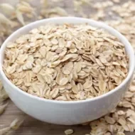 Bowl branco com aveia e grãos de aveia em volta.