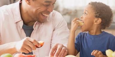 Lanche da Tarde: 20 receitas práticas para sair do básico!  Lanche da Tarde: Um homem negro com uma maçã na mão e uma criança negra comendo uma maçã