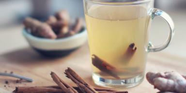 Chá de Gengibre: chá de gengibre em uma xícara, com canela dentro e em volta da xícara, em cima de uma mesa de madeira