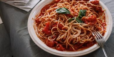 Opções de almoço rápido e fácil:Macarrão com molho de tomate no prato com um garfo ao lado em cima de uma mesa com pano cinza