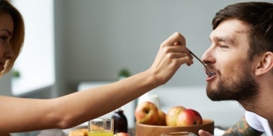 Café da Manhã Romântico: Mulher à esquerda colocando uma colher com comida na boca de um homem à direita