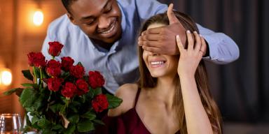 Um homem cobre os olhos de sua namorada para lhe entregar um buquê de flores.