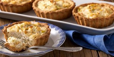 Quiche de alho-poró sendo cortado sobre um prato com um garfo ao lado. Ao fundo, mais 3 quiches inteiros
