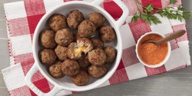 Panela com vários bolinhos de carne moída recheados com queijo. À direita um molho e, abaixo, um pano xadrez (Vermelho e bran