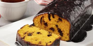 Bolo de cenoura com cobertura de chocolate em cima de um prato, à esquerda pote com gotas de chocolate