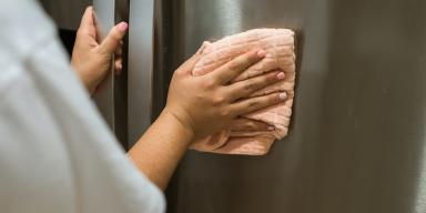 Mulher limpando a geladeira inox com um pano laranja