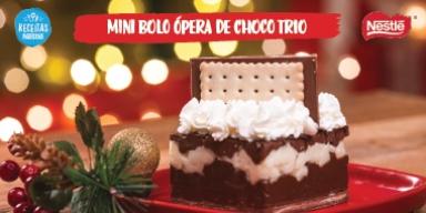 Fotografia de um bolo com três camadas com chantilly e um biscoito no topo. O bolo está sobre um prato vermelho.