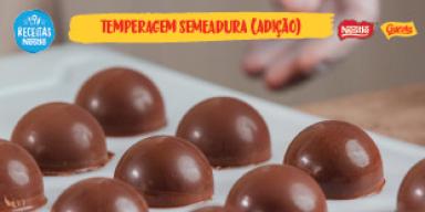 Imagem bastante aproximada de bombons caseiros de chocolate brilhantes sobre papel manteiga com o título do vídeo acima