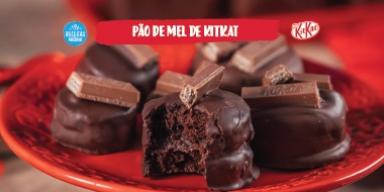 Fotografia mostra uma bancada de madeira e um prato vermelho redondo ao centro. Em cima, pães de mel de chocolate com KitKat.
