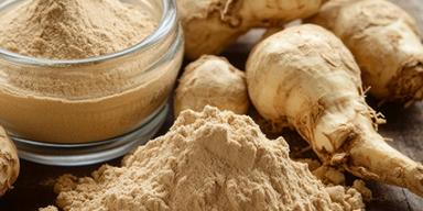 Raízes de maca peruana e pó em recipiente e montinho sobre mesa rústica de madeira.