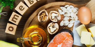 Alimentos ricos em ômega-3 sobre uma tábua: salmão, abacate, ovos, oleaginosas, azeite, manteiga e brócolis.