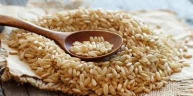 Arroz integral cru sobre tecido rústico, com colher de madeira apoiada por cima, em uma superfície de madeira envelhecida.