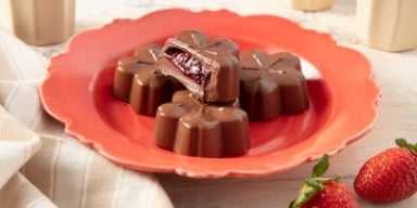 Chocolate ao leite: receitas de dar água na boca! Imagem de bombons de chocolate em formato de flor com recheio de morango sobre um prato vermelho.