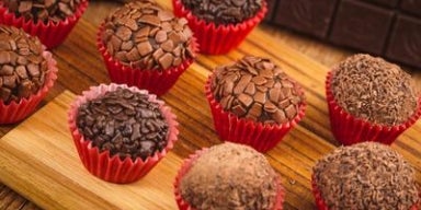 Docinhos para festa Imagem de brigadeiros de chocolate em forminhas vermelhas em uma tábua de madeira.