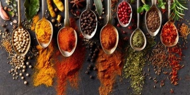 O que são condimentos e como usá-los na cozinha? Colheres com diferentes temperos e especiarias coloridas espalhadas sobre superfície escura.