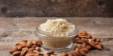 Farinha de amêndoas: benefícios, nutrientes e como usar Pote de vidro com farinha de amêndoas, cercado por amêndoas cruas sobre superfície de madeira rústica.