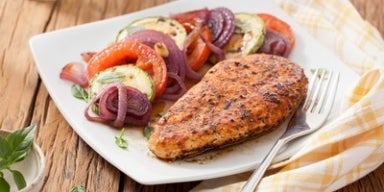 Filé de frango grelhado suculento com legumes grelhados em um prato branco.