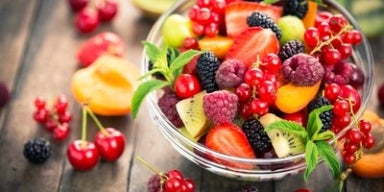 Frutas ricas em proteínas Tigela de vidro com frutas coloridas como framboesas, kiwis, cerejas, pêssego, groselha e amora.